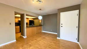 Kitchen featuring dark countertops, decorative light fixtures, black appliances, light wood-style flooring, and a peninsula