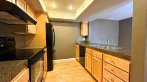 Kitchen with tile countertops, black appliances, under cabinet range hood, light wood-style floors, and a raised ceiling