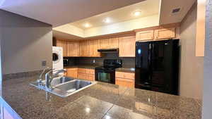 Kitchen with tile countertops, black appliances, light brown cabinetry, a textured wall, and recessed lighting