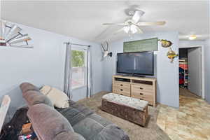 Living room featuring a textured ceiling, light colored carpet, a ceiling fan, and lofted ceiling