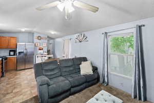 Living room featuring lofted ceiling, a textured ceiling, ceiling fan, and light carpet