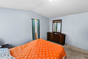 Carpeted bedroom featuring vaulted ceiling and a textured ceiling