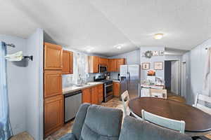 Kitchen with stainless steel appliances, light countertops, vaulted ceiling, a textured ceiling, and stone finish flooring