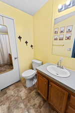 Bathroom with a textured ceiling, vanity, stone finish floors, and a shower with curtain