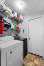 Laundry area with stone finish floors, a textured ceiling, and washing machine and dryer