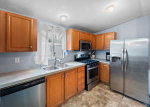 Kitchen with appliances with stainless steel finishes, a textured ceiling, light countertops, brown cabinets, and vaulted ceiling