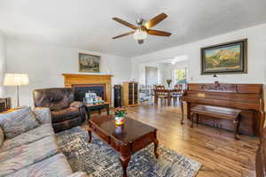 Living room with wood-type flooring, ceiling fan, a fireplace, and a textured ceiling