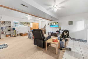 Living room featuring a ceiling fan, beam ceiling, light tile patterned flooring, light colored carpet, and electric panel