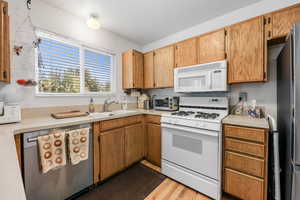 Kitchen featuring stainless steel appliances, light countertops, dark wood finished floors, and brown cabinets