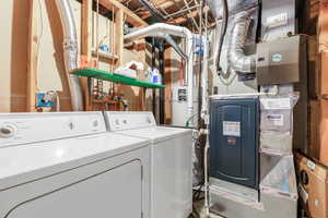 Washroom featuring heating unit, water heater, and washer and clothes dryer