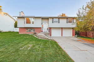 Bi-level home featuring brick siding, driveway, a chimney, and an attached garage