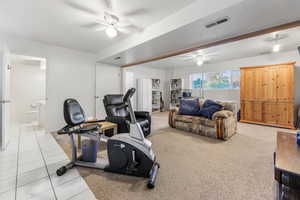Exercise area with a ceiling fan, light tile patterned floors, a textured ceiling, and light colored carpet