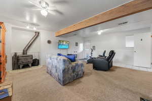 Living area featuring a wood stove, light tile patterned flooring, beam ceiling, a textured ceiling, and a ceiling fan