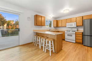 Kitchen featuring a breakfast bar area, white appliances, light countertops, a peninsula, and light wood-style flooring