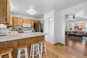 Kitchen featuring light countertops, a kitchen bar, light wood-style floors, a peninsula, and white appliances