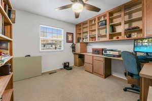 Office space with built in study area, light colored carpet, and ceiling fan