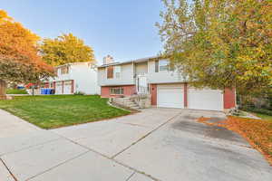 Split foyer home with brick siding, a front yard, a chimney, driveway, and an attached garage