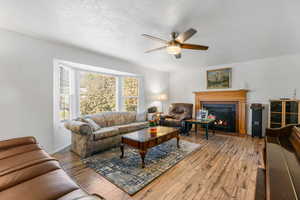 Living room featuring a textured ceiling, hardwood / wood-style flooring, a lit fireplace, and ceiling fan