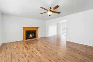 Living room with a fireplace, wood finished floors, and a ceiling fan