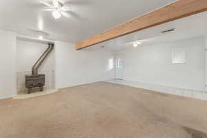 Basement family room, walk-out area with a wood stove, a ceiling fan, and light carpet