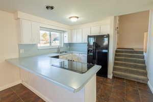 Kitchen featuring a peninsula, light countertops, black appliances, and white cabinetry
