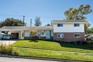 Tri-level home featuring a front yard, brick siding, and concrete driveway