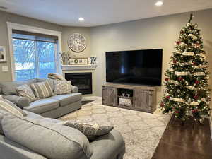 Living room with dark wood-type flooring, a glass covered fireplace, and recessed lighting