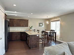 Kitchen with a peninsula, a kitchen breakfast bar, dark brown cabinetry, light stone counters, and black appliances