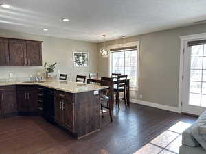 Kitchen featuring a kitchen breakfast bar, dark brown cabinets, light stone countertops, a peninsula, and a textured ceiling