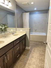 Full bath featuring a textured ceiling, double vanity, light tile patterned floors, and shower / tub combo with curtain