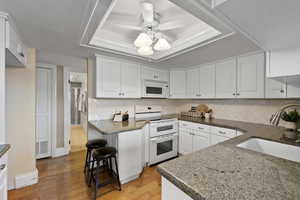 Kitchen featuring a tray ceiling, white appliances, light wood-type flooring, white cabinets, and decorative backsplash