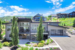 View of front of house featuring stone siding, driveway, an attached garage, and a balcony