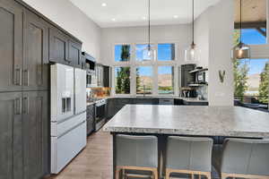 Kitchen featuring white fridge with ice dispenser, decorative light fixtures, a kitchen breakfast bar, tasteful backsplash, and a high ceiling