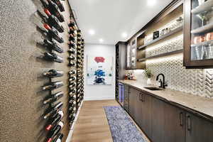 Wine area featuring light wood-style flooring, wet bar, wine cooler, and recessed lighting