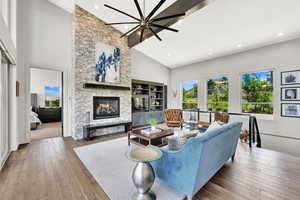 Living area with a stone fireplace, wood-type flooring, high vaulted ceiling, and recessed lighting