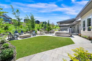 View of green lawn with a patio area, a hot tub, and a fire pit