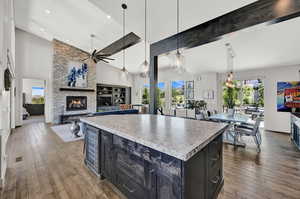 Kitchen with dark cabinetry, decorative light fixtures, light wood finished floors, a center island, and high vaulted ceiling