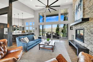 Living room featuring a stone fireplace, wood finished floors, a mountain view, a towering ceiling, and recessed lighting