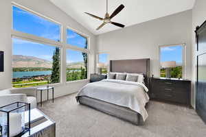 Bedroom with a barn door, high vaulted ceiling, a water and mountain view, light colored carpet, and a ceiling fan
