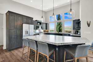 Kitchen with a kitchen bar, dark wood-style floors, hanging light fixtures, stainless steel appliances, and a high ceiling