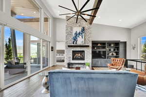 Living area featuring a stone fireplace, hardwood / wood-style floors, a chandelier, a high ceiling, and recessed lighting