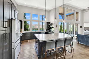 Kitchen with a towering ceiling, a kitchen breakfast bar, decorative light fixtures, light wood-style flooring, and a kitchen island