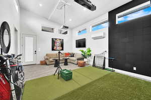 Living room featuring recessed lighting, a towering ceiling, a wall mounted AC, and golf simulator