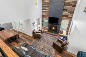Living room featuring dark wood-style floors, a towering ceiling, a large fireplace, and healthy amount of natural light