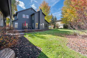 Back of house featuring a deck, a chimney, and a lawn