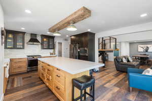Kitchen featuring glass insert cabinets, stainless steel appliances, wall chimney exhaust hood, a kitchen breakfast bar, and decorative backsplash