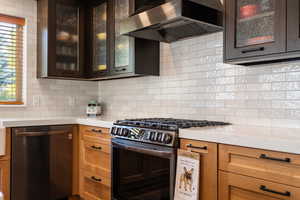 Kitchen featuring glass insert cabinets, gas stove, black dishwasher, exhaust hood, and backsplash