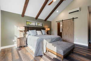 Bedroom with high vaulted ceiling, beamed ceiling, ensuite bath, a barn door, and a wall mounted air conditioner