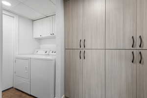 Washroom with cabinet space, washing machine and dryer, a drop ceiling, and dark wood-type flooring