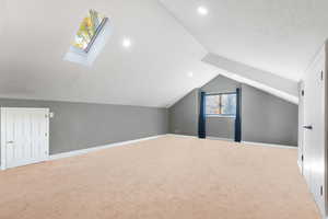 Bedroom 3 with no furniture, space featuring carpet flooring, vaulted ceiling, a skylight, and recessed lighting